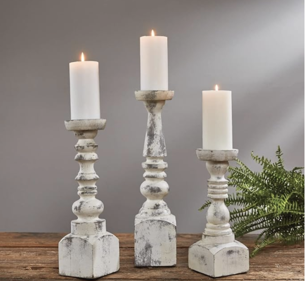 Three white candle holders on a wooden table, perfect for farmhouse or rustic decor.